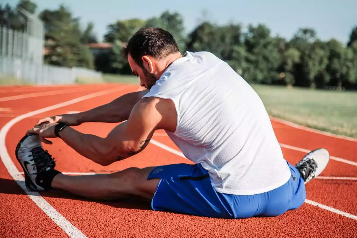 Hombre estirando sus piernas en una pista de atletismo