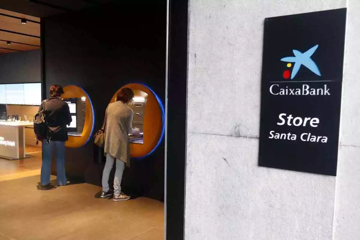Imagen de dos clientes de CaixaBank sacando dinero de una central en Barcelona, en Cataluña