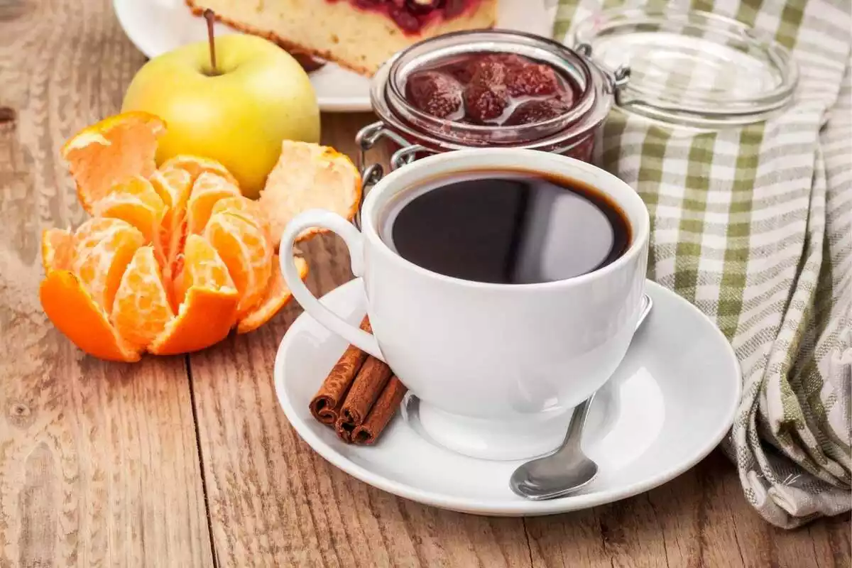 Una taza de café junto a una mandarina y otros alimentos del desayuno