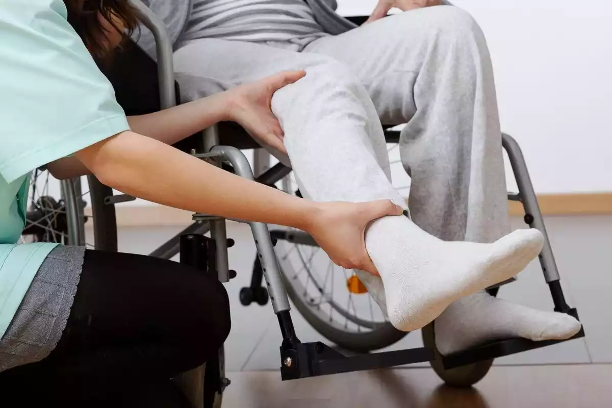 Fisioterapeuta realizando ejercicio en las piernas de una persona parapléjica en una silla de ruedas