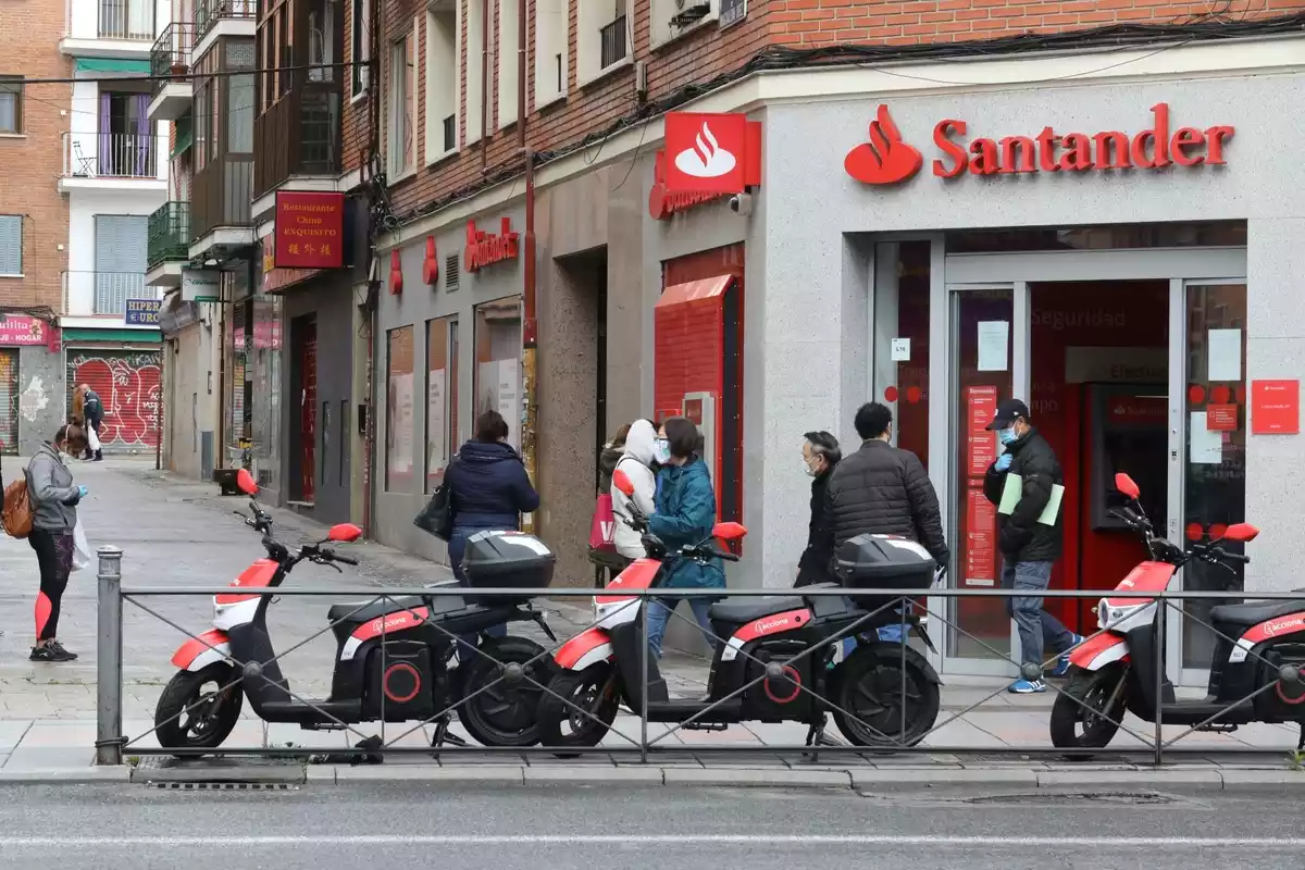 Varias personas esperan para entrar a una oficina del Banco Santander durante el inicio de la cuarta semana del estado de alarma