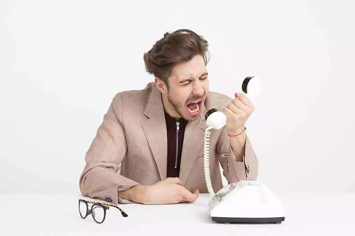 Hombre gritando al teléfono con gafas en la mesa