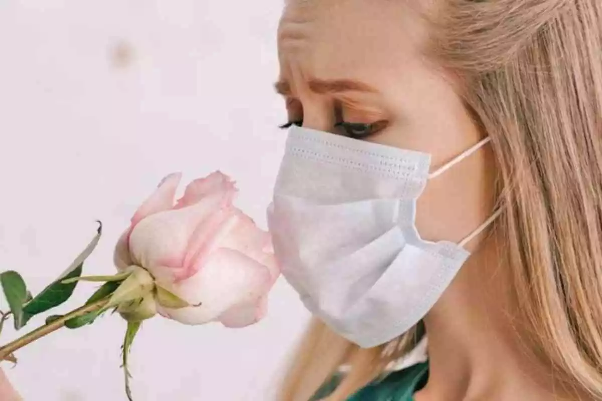 Mujer con mascarilla oliendo una flor