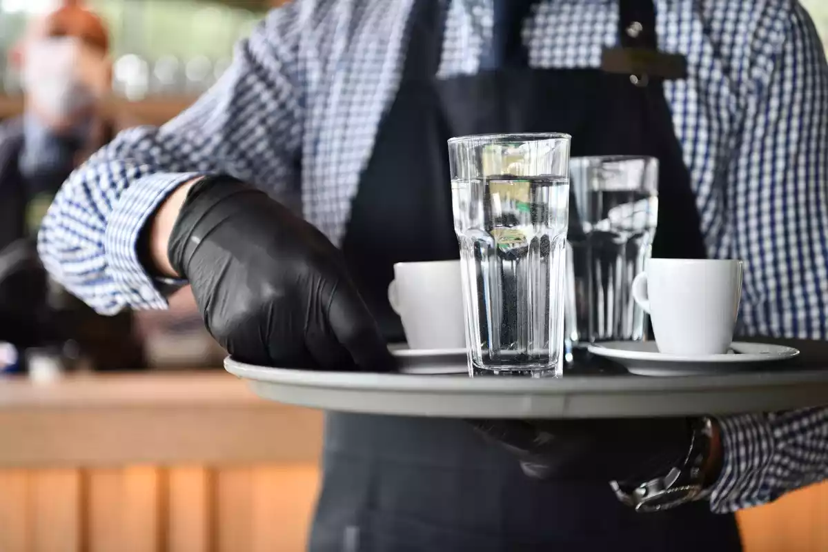 Un camarero con guantes sirve unas bebidas
