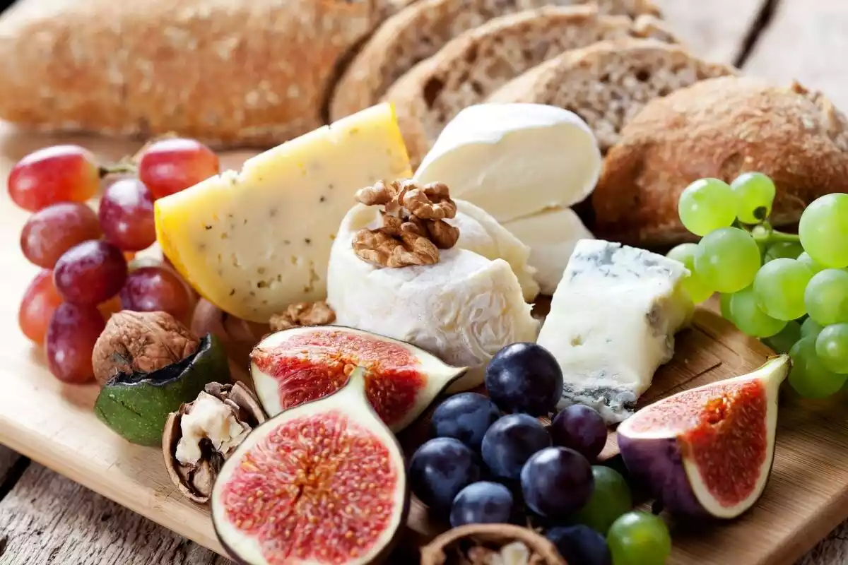 Higos, queso, frutos secos, pan y uvas sobre una mesa de madera