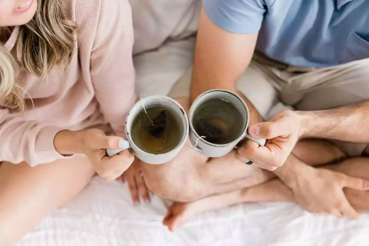 Un hombre y una mujer con dos tazas de tés en una cama