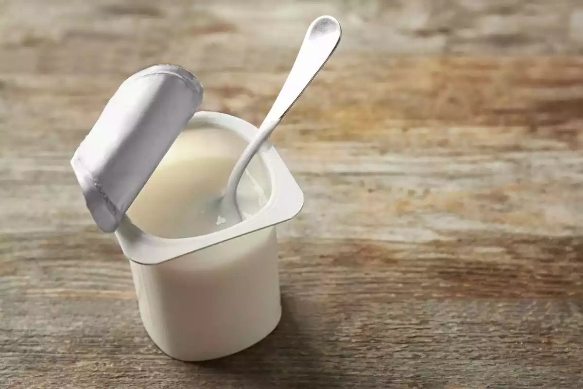 Un yogur blanco con cuchara dentro sobre una mesa de madera