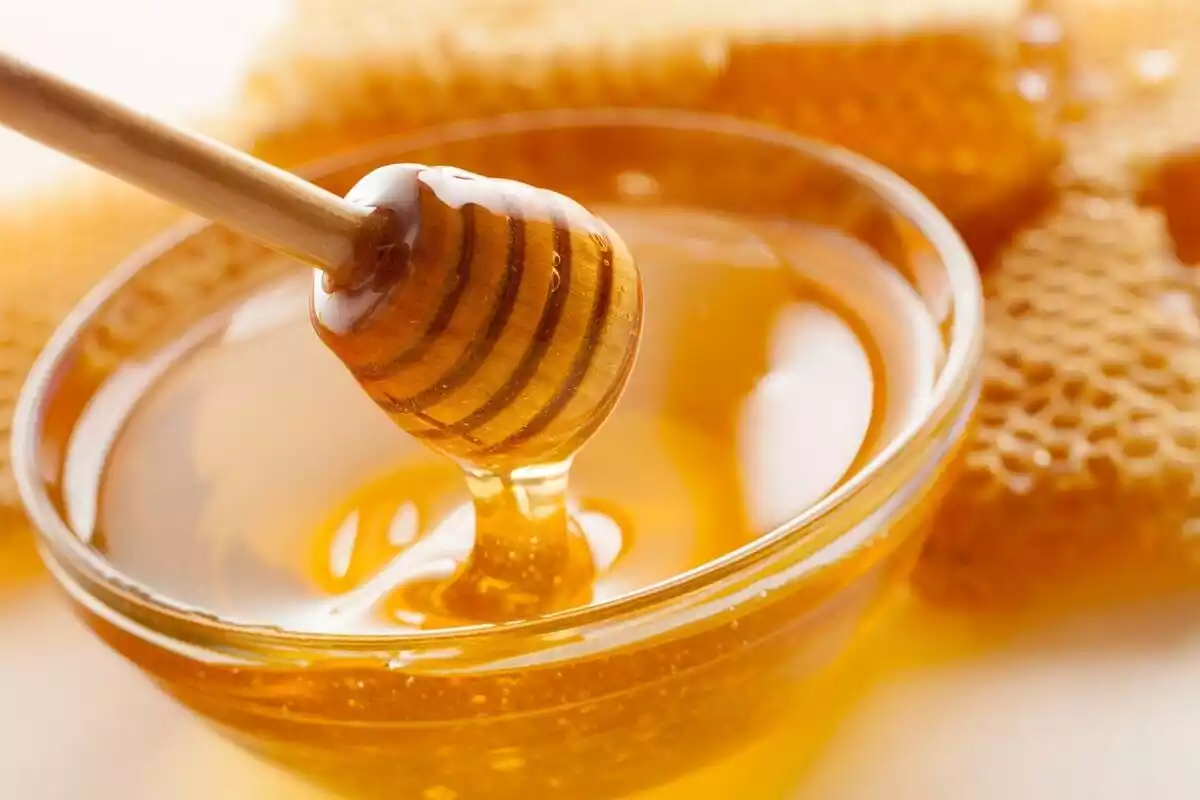 Una cuchara de miel en un vaso lleno de miel y panales detrás