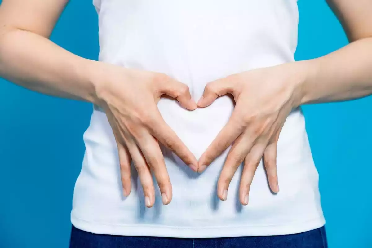 Una mujer haciendo un corazón a la zona del estómago con sus dedos
