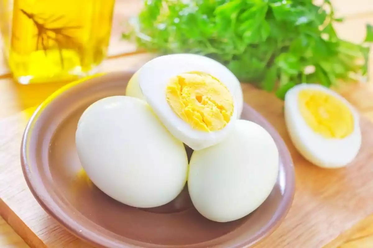 Varios huevos blancos cocidos con la yema amarilla a la vista y perejil detrás