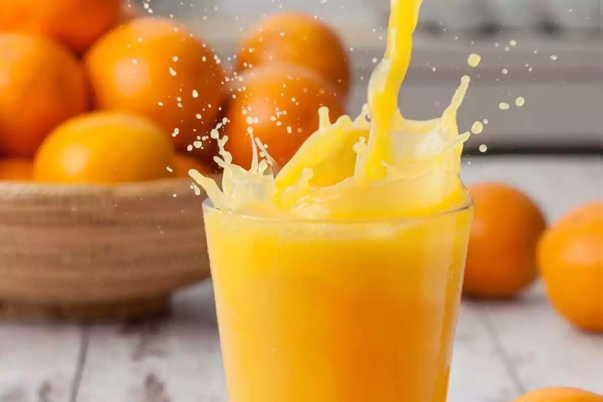 Zumo de naranja exprimido en un vaso con varias frutas detrás