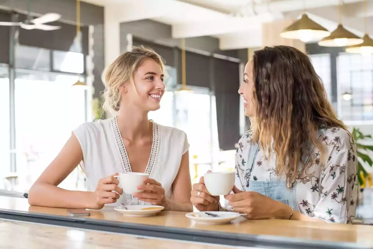 Dos mujeres conversando con dos tazas de café en la mano