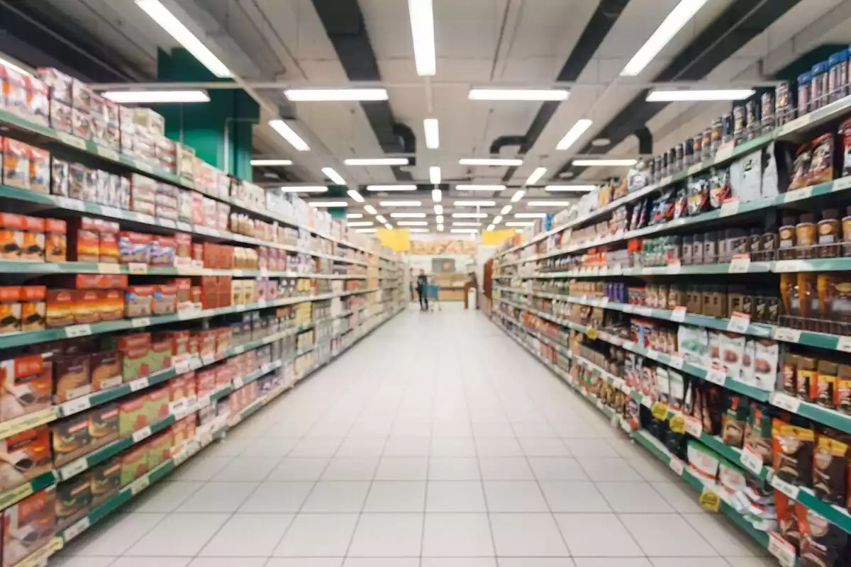 Pasillo largo de supermercado con estanterías llenas de productos y una persona al fondo