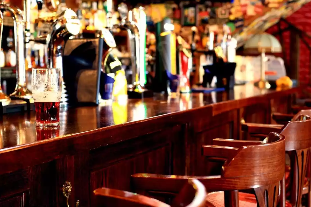 Plano general de la barra de un bar con sillas de madera y cerveza