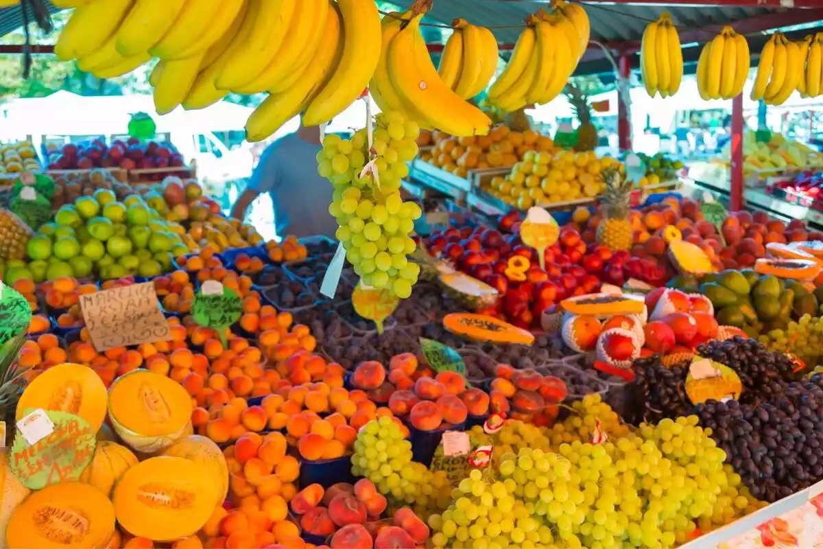 Puesto de frutas en un mercado con plátanos, uvas, melones, melocotones, manzanas y más