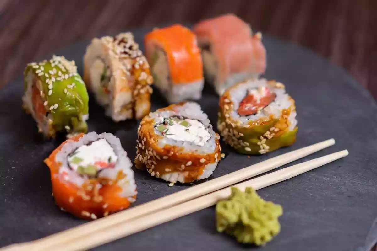 Siete trozos de sushi con dos palillos y algo de wasabi en un plato negro
