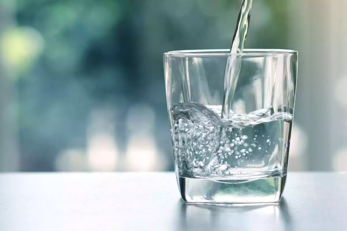 Un vaso de agua transparente sobre una mesa de cristal con un chorro de agua cayendo