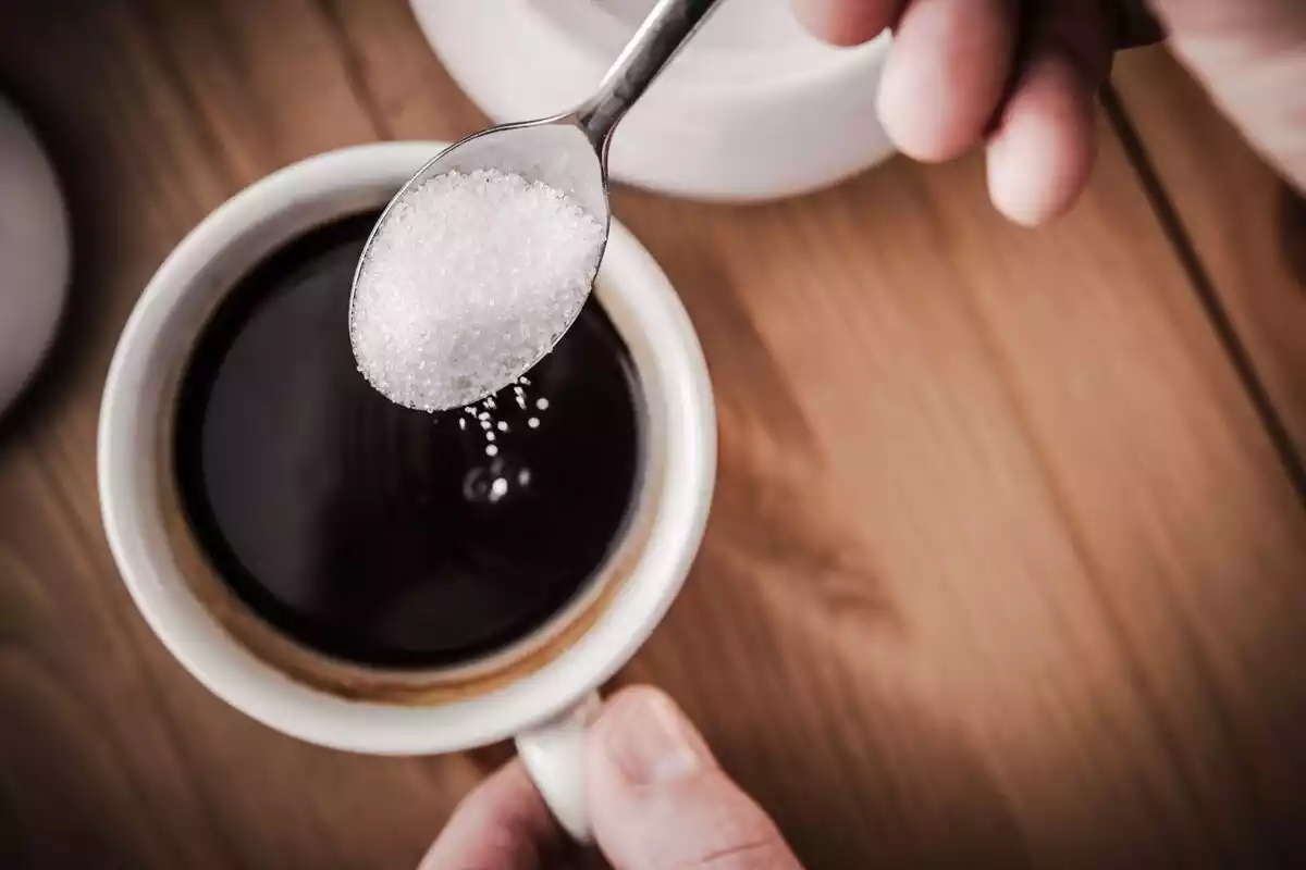 Una cucharita de azúcar encima de una taza de café oscuro sobre una mesa