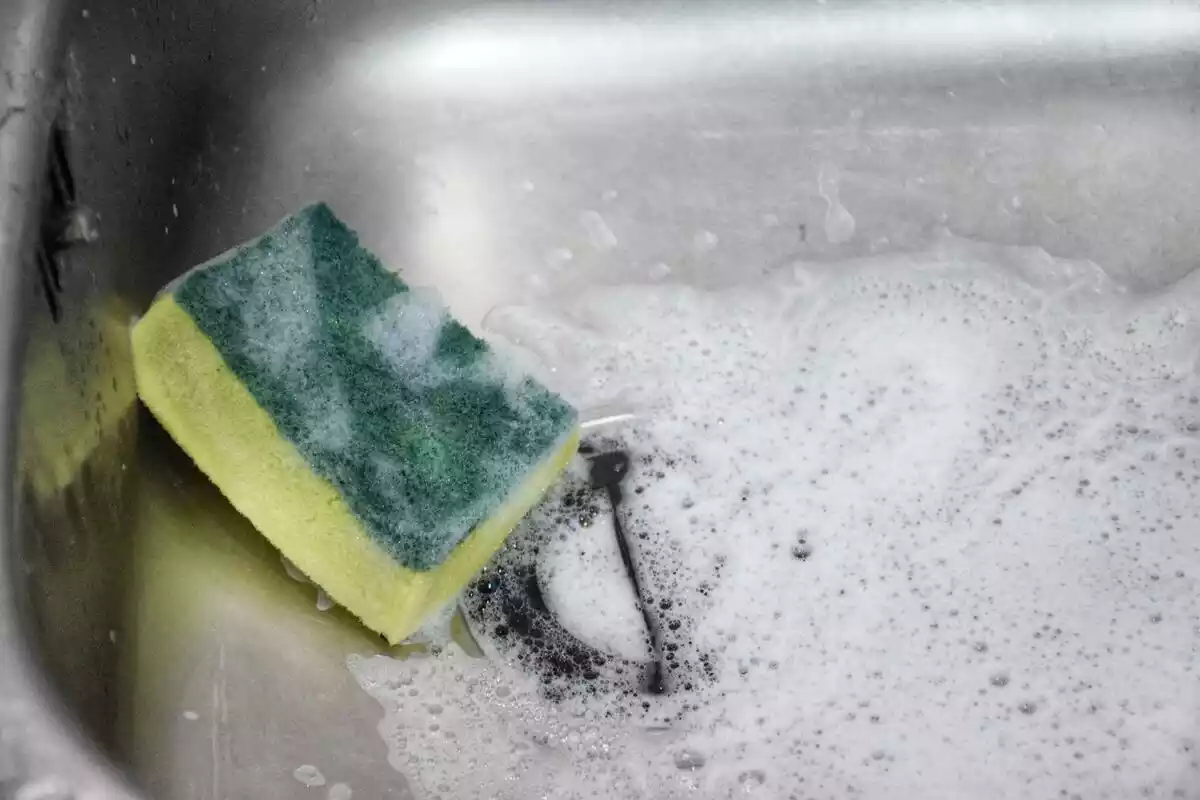 Una esponja de color verde y amarillo con espuma en un fregadero