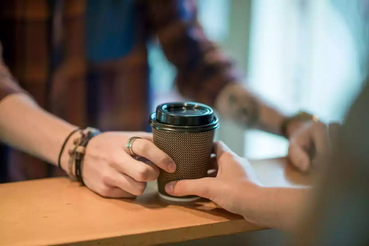 Una mano cogiendo un café para llevar encima de un soporte de madera