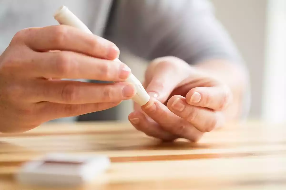 Una mano con una prueba de glucosa pinchando un dedo sobre una mesa de madera