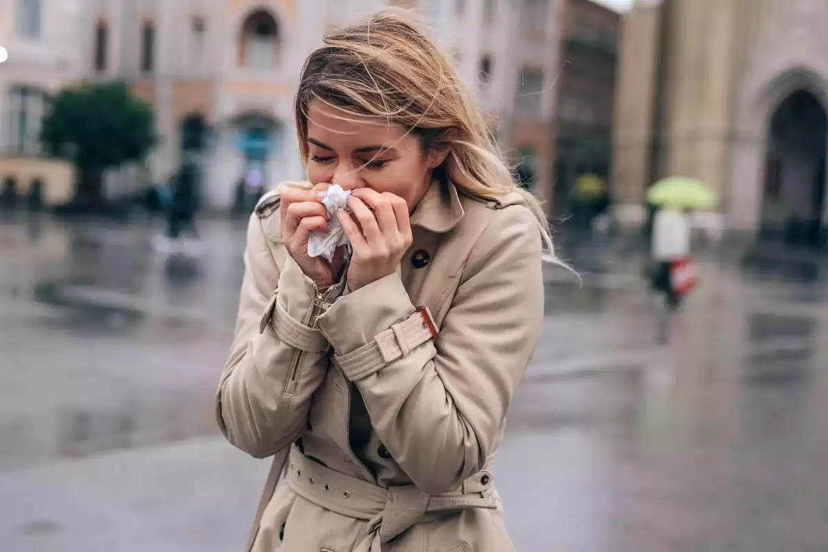 Una mujer con abrigo de color gris se lleva las manos a la nariz con un pañuelo