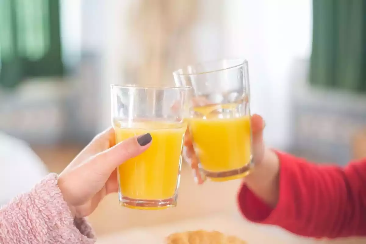 Dos personas sujetando un vaso con zumo de naranja