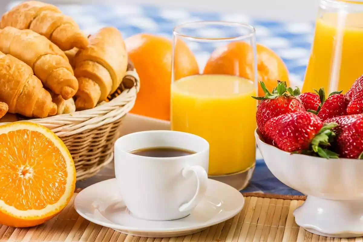 Mesa con café, zumo de naranja, naranjas, fresas y bollería