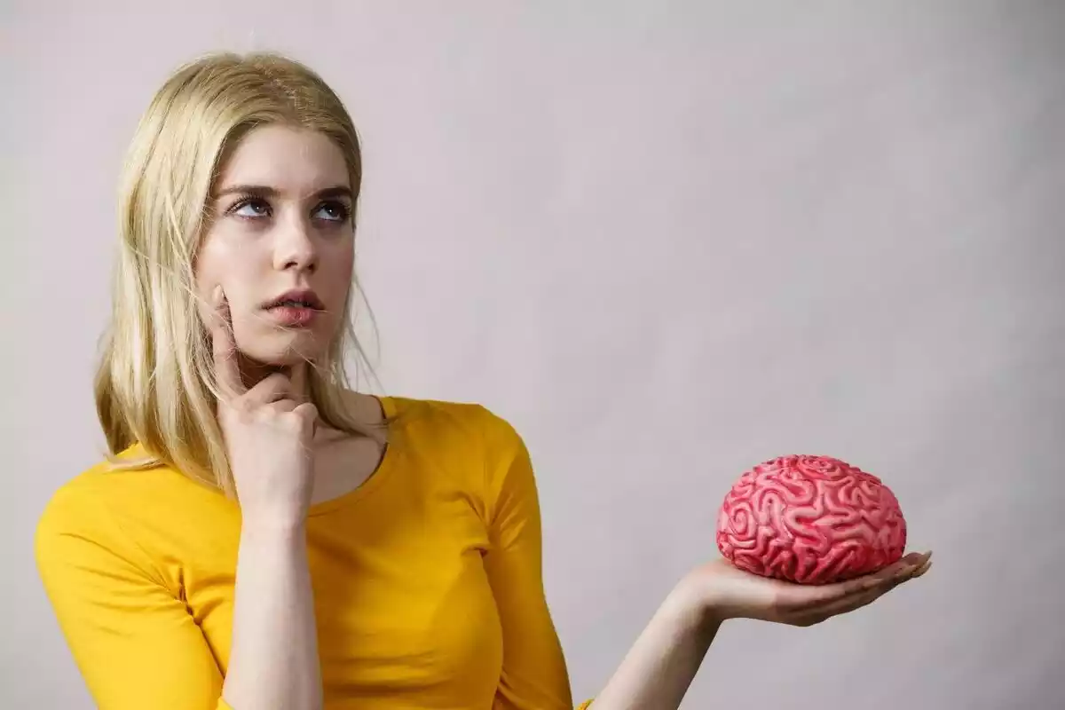 Mujer sujetando en una mano un cerebro y con la otra mostrando un gesto de duda