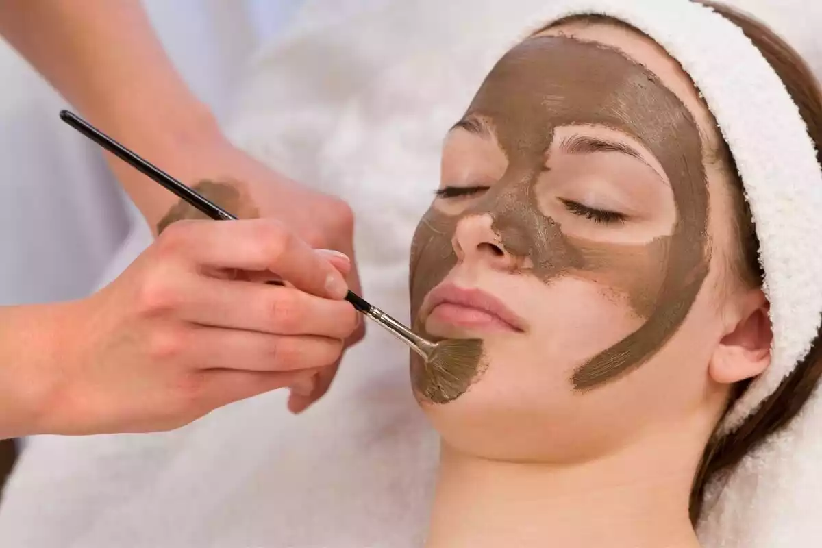 Persona aplicando mascarilla de chocolate con un pincel a una mujer