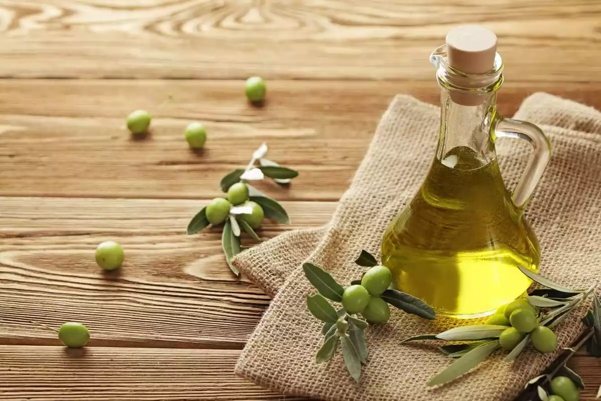 Recipiente con aceite de oliva sobre un paño acompañado con olivas
