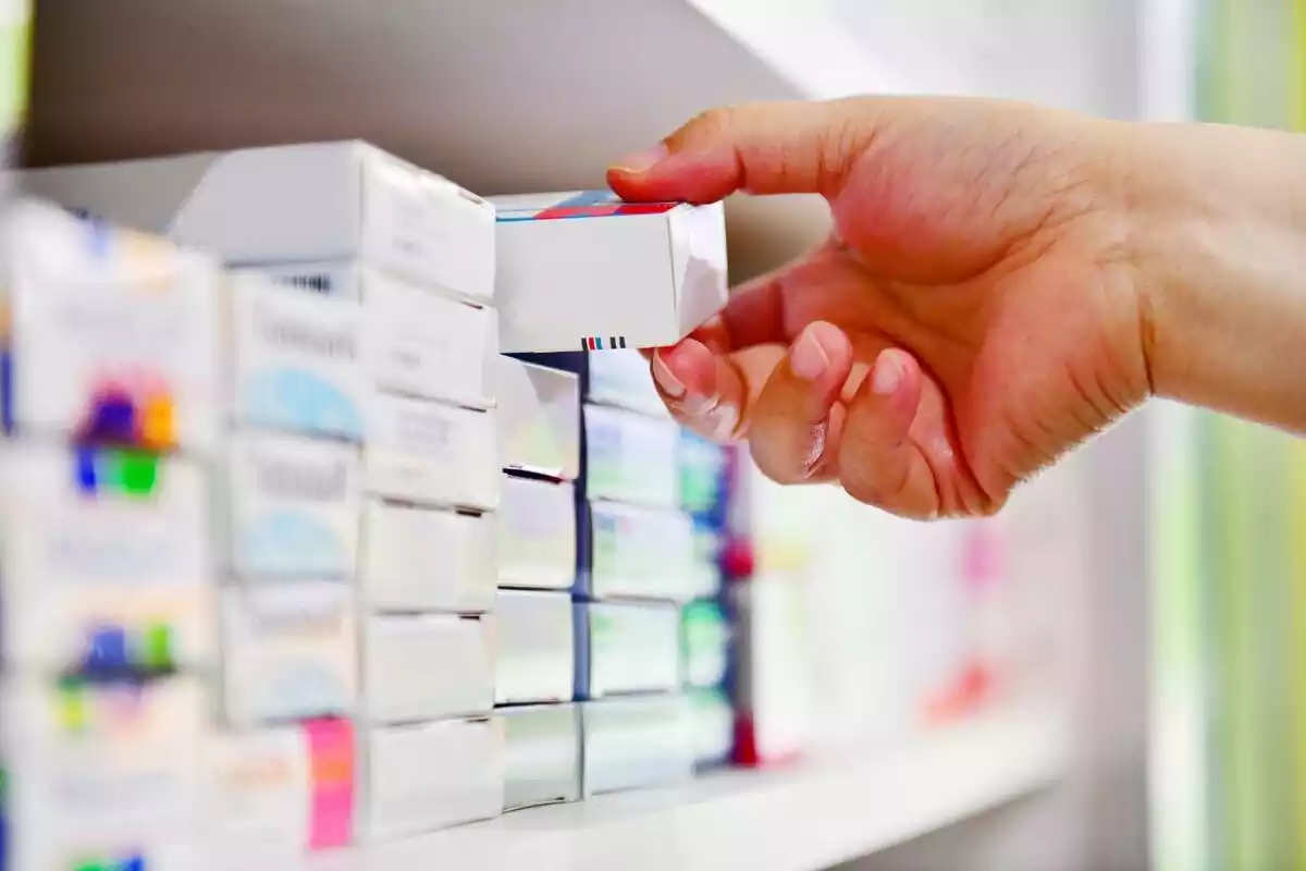 Una farmacéutica cogiendo una caja de medicamentos de una estantería