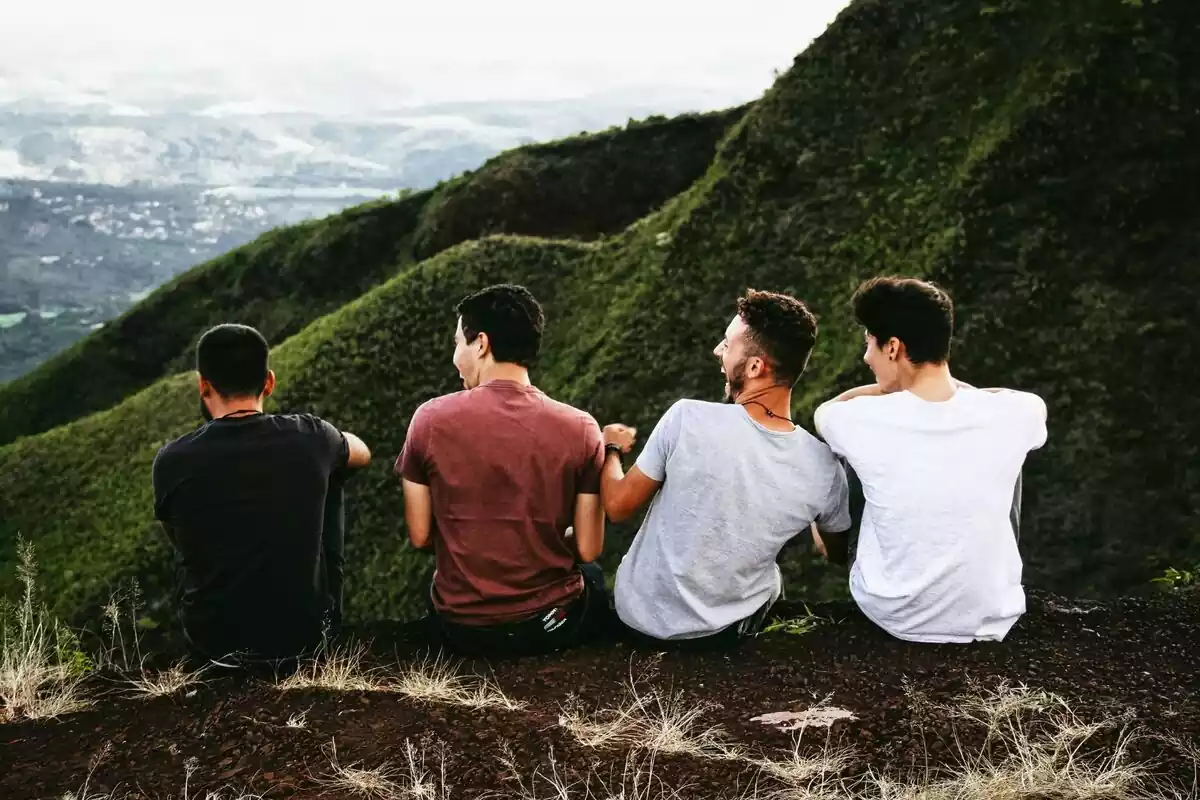 Grupo de chicos de espaldas, sentados sobre tierra en una montaña