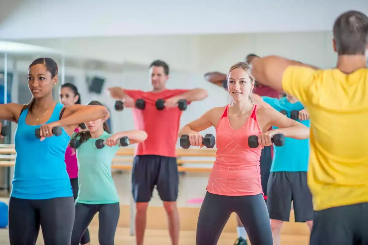 Grupo de personas sosteniendo pesas mientras practican ejercicio en un gimnasio