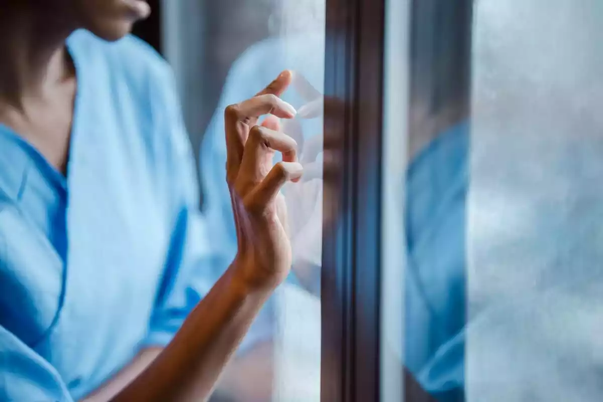 Médica apoyando una mano en la ventana de un hospital