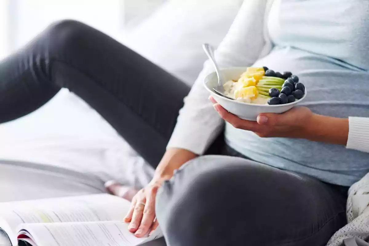 Mujer embarazada comiendo un bol de yogur y frutas