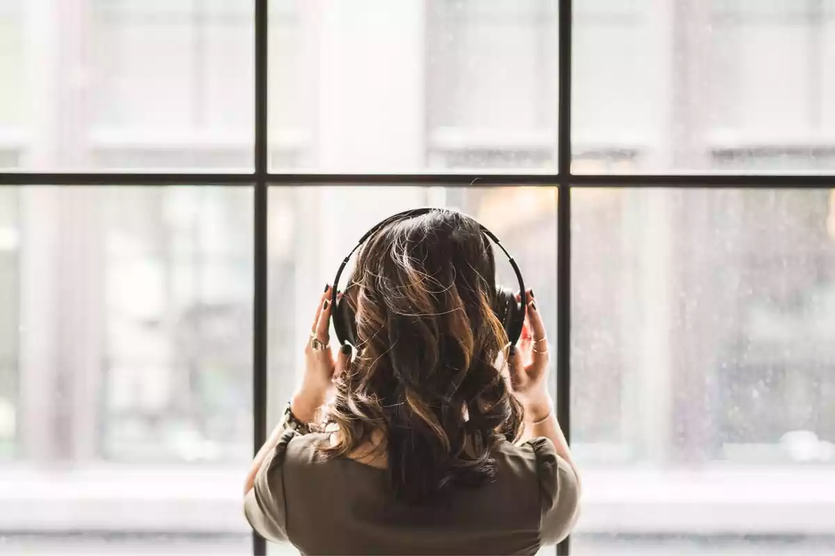 Mujer mirando por la ventana mientras escucha música con unos auriculares