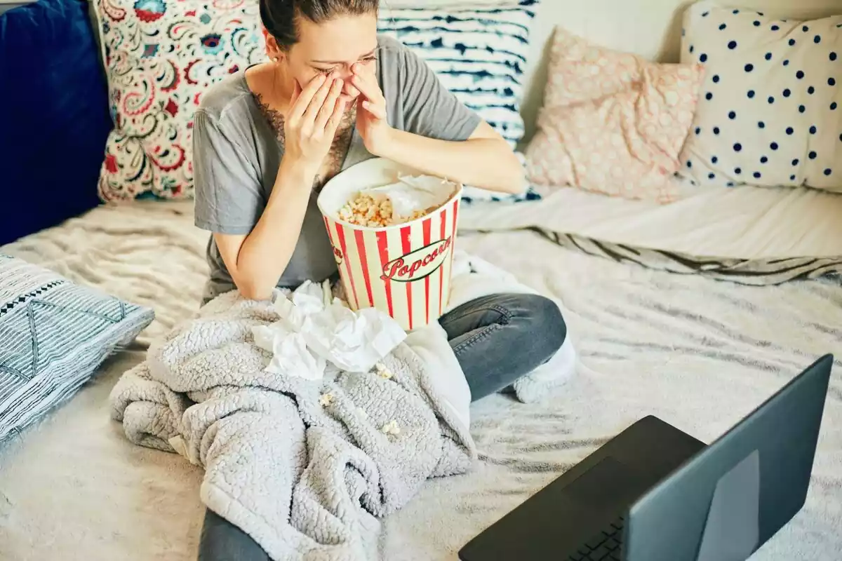 Mujer viendo una película triste en el ordenador mientras se limpia las lágrimas