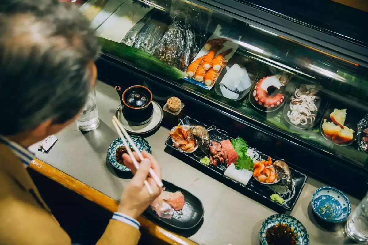 Un hombre comiendo sushi con palillos en un restaurante japonés