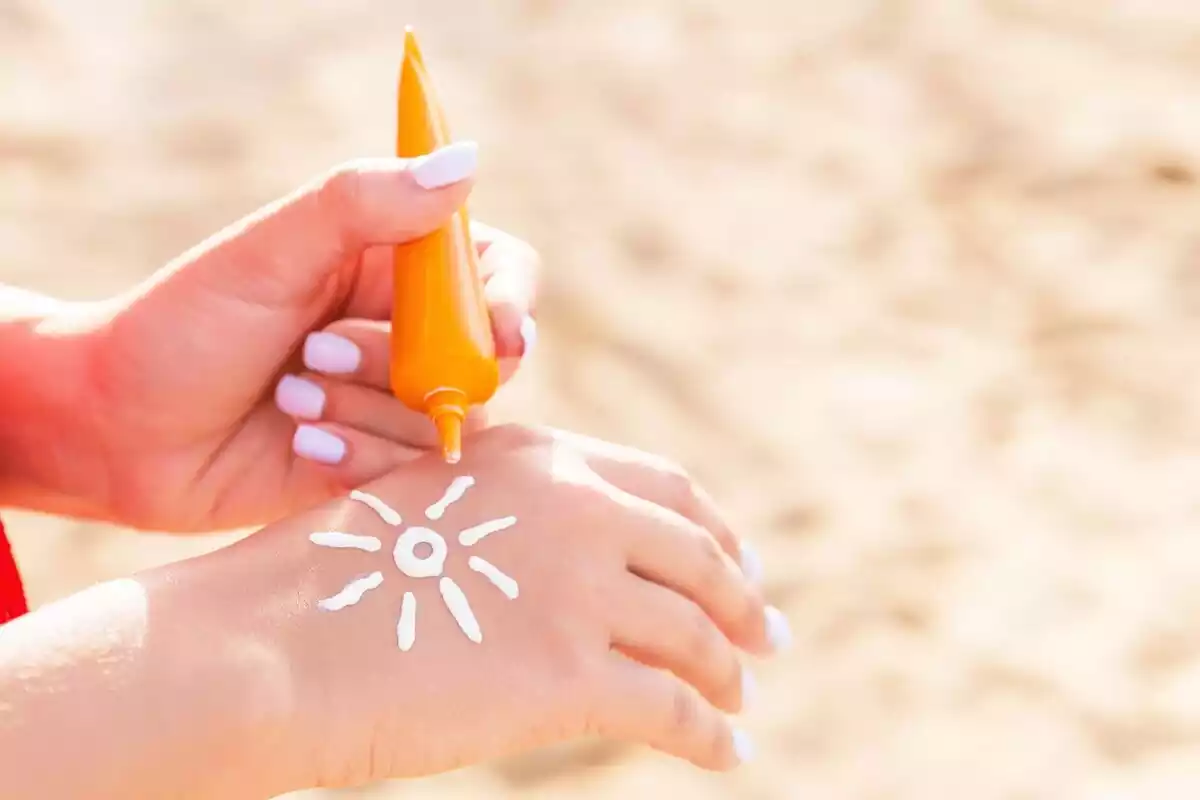 Una mano sujetando una crema solar naranja en la playa