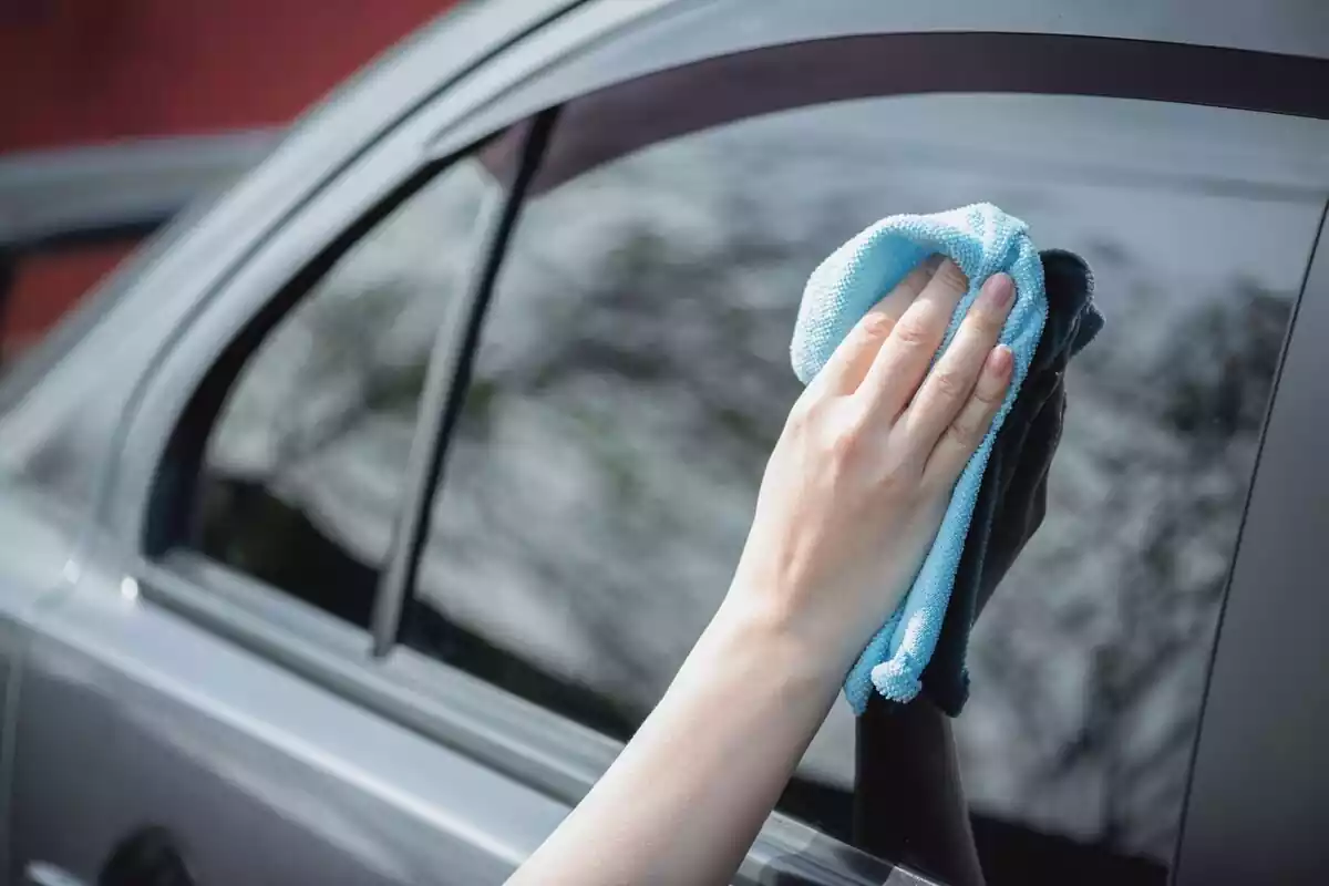 Mano limpiando con una bayeta la ventana de un coche