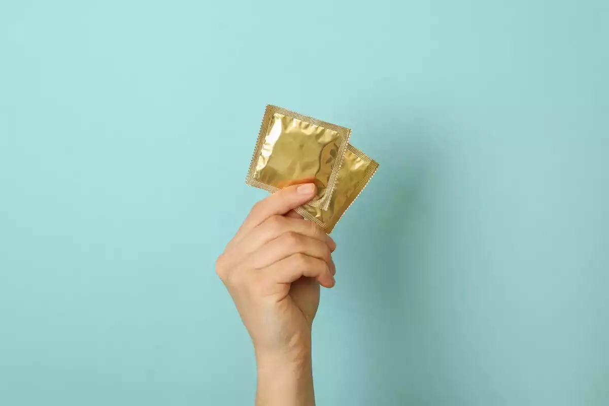 Mano sosteniendo unos preservativos dorados