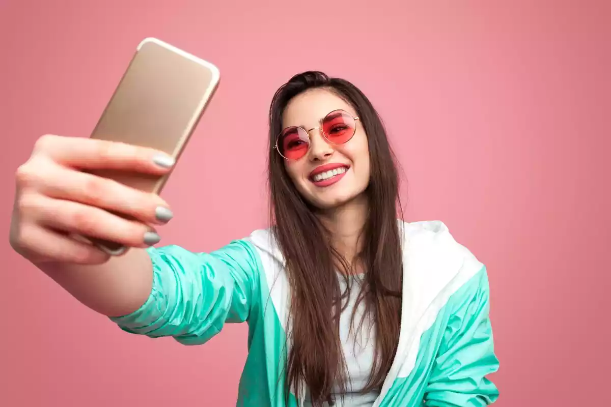 Mujer haciéndose un selfie con un fondo rosado