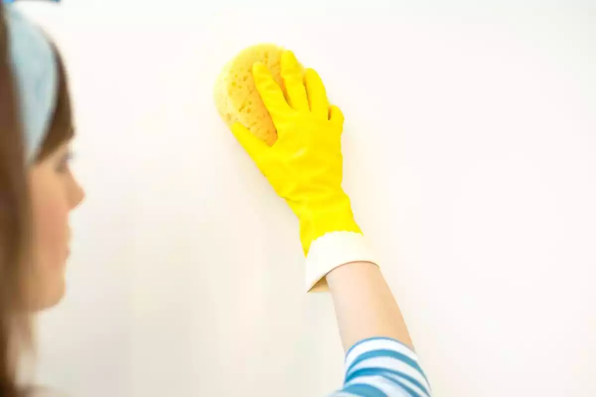 Mujer limpiando una pared blanca con una esponja