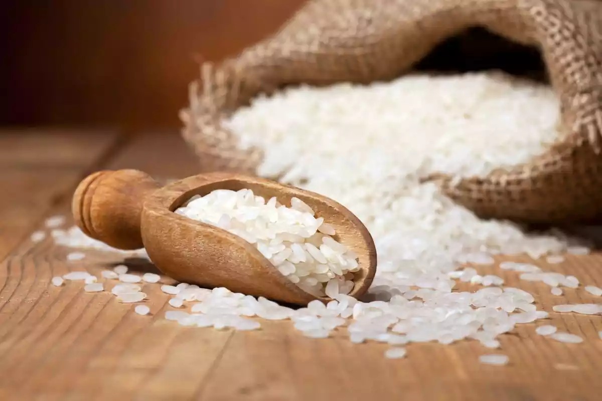 Saco de arroz blanco abierto y una cuchara al lado sobre una mesa de madera