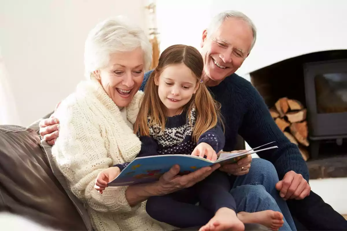 Un abuelo y una abuela con su nieta en el sofá leyendo un libro