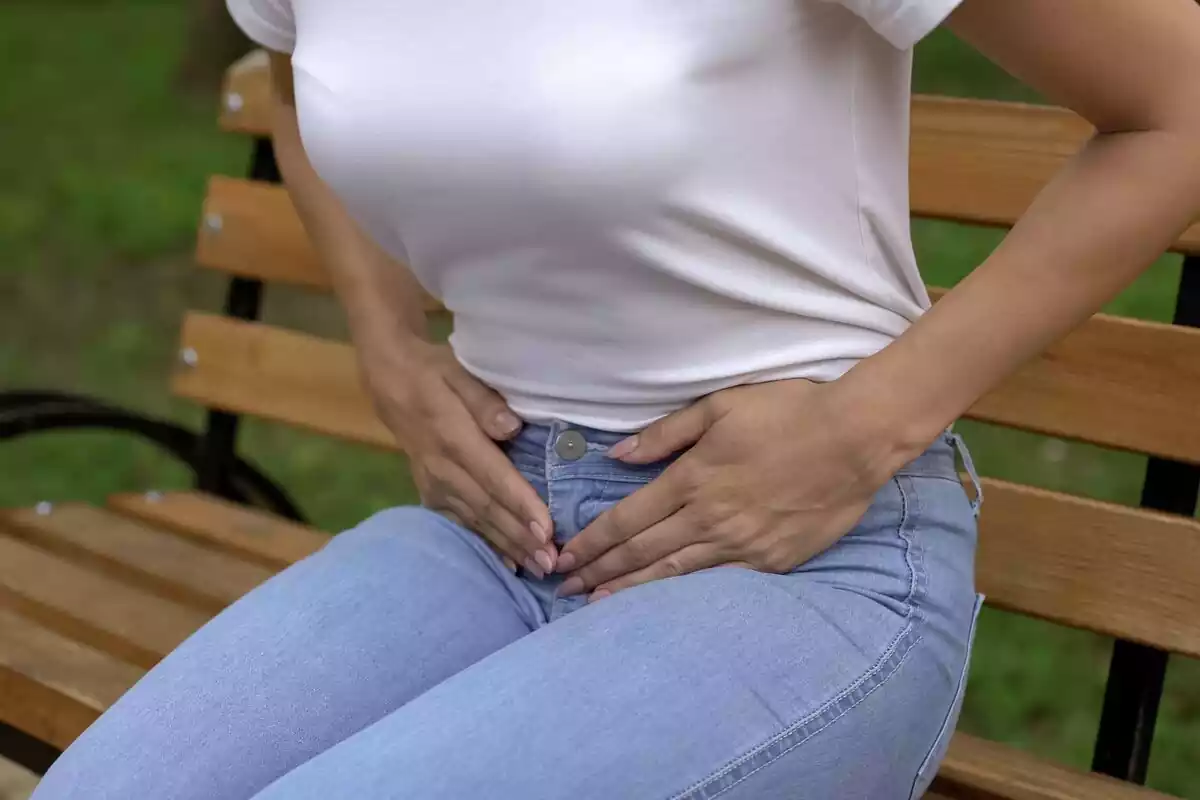 Una mujer con tejanos y camiseta blanca tocándose la parte abdominal