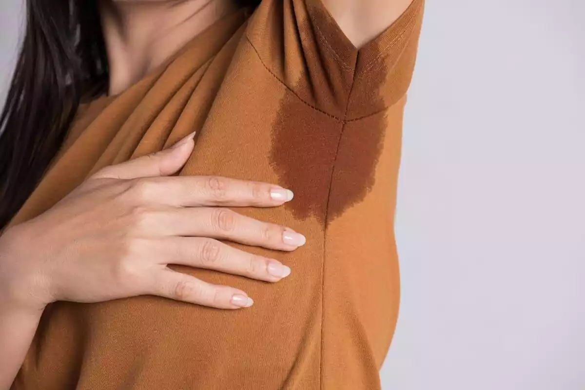 Una mujer enseñando con la mano una mancha de sudor en su sobaco