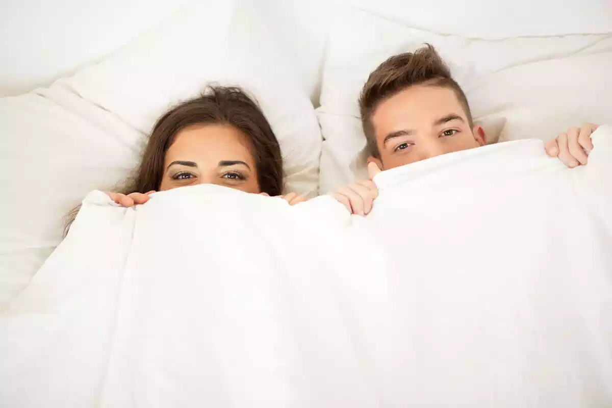 Una pareja cubriéndose la cara con el edredón de la cama