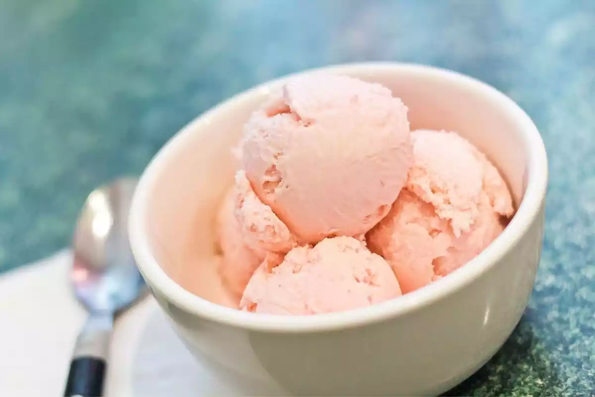 Varias bolas de helado rosa en un bol junto a una cuchara